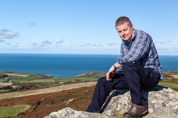 Portrait of Ian Stacey, landscape and property photographer, sitting on rock overlooking coast in Pembrokeshire