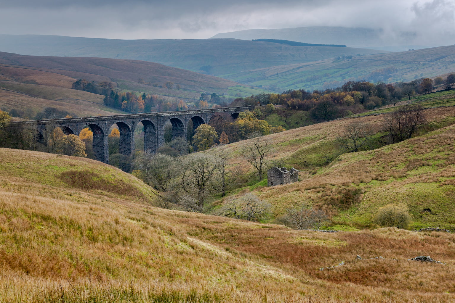 A landscape photograph of the Dent Head Viaduct on the Settle to Carlisle railway line in Dentdale, Cumbria with derelict stone barn in foreground.