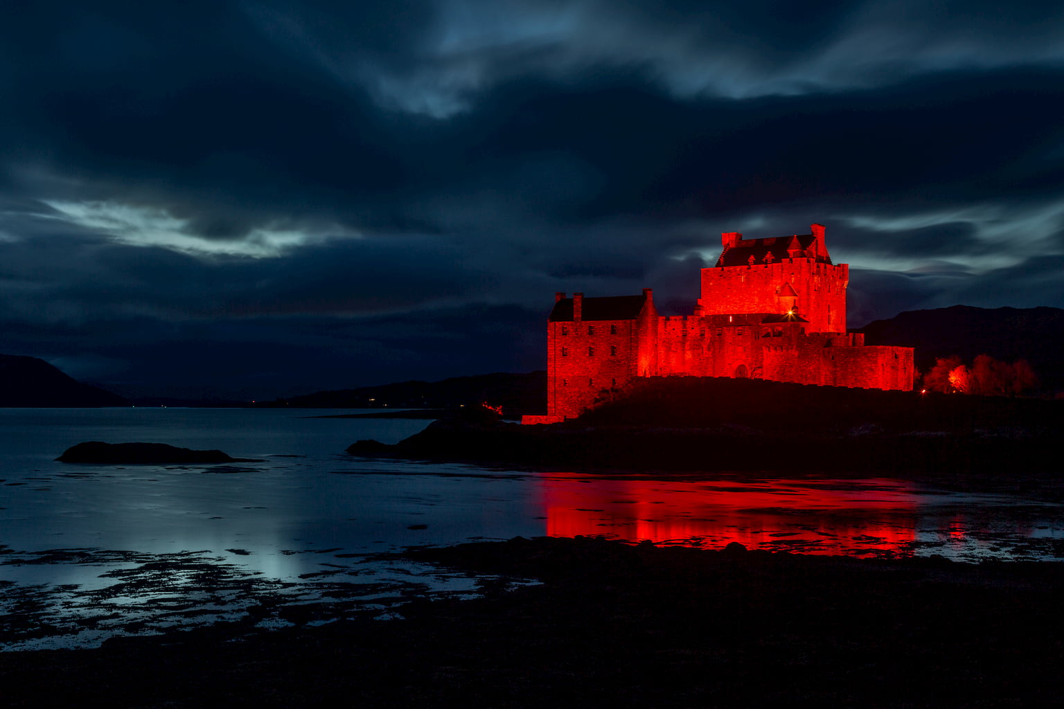 A landscape photograph of Eilean Donan castle in the Western Highlands of Scotland at night while lit up in red.